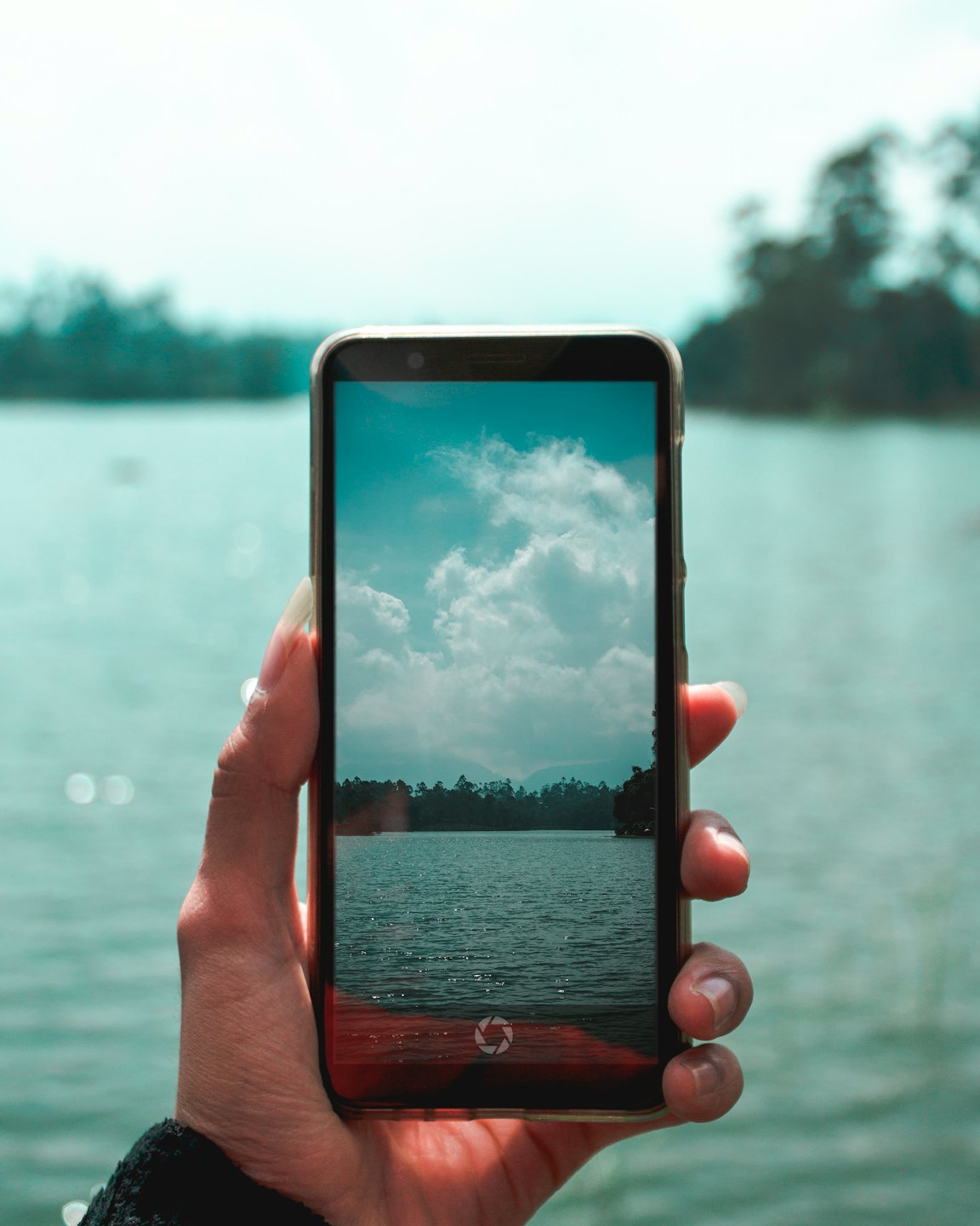 Eine Hand hält ein Smartphone und filmt eine malerische Seenlandschaft.