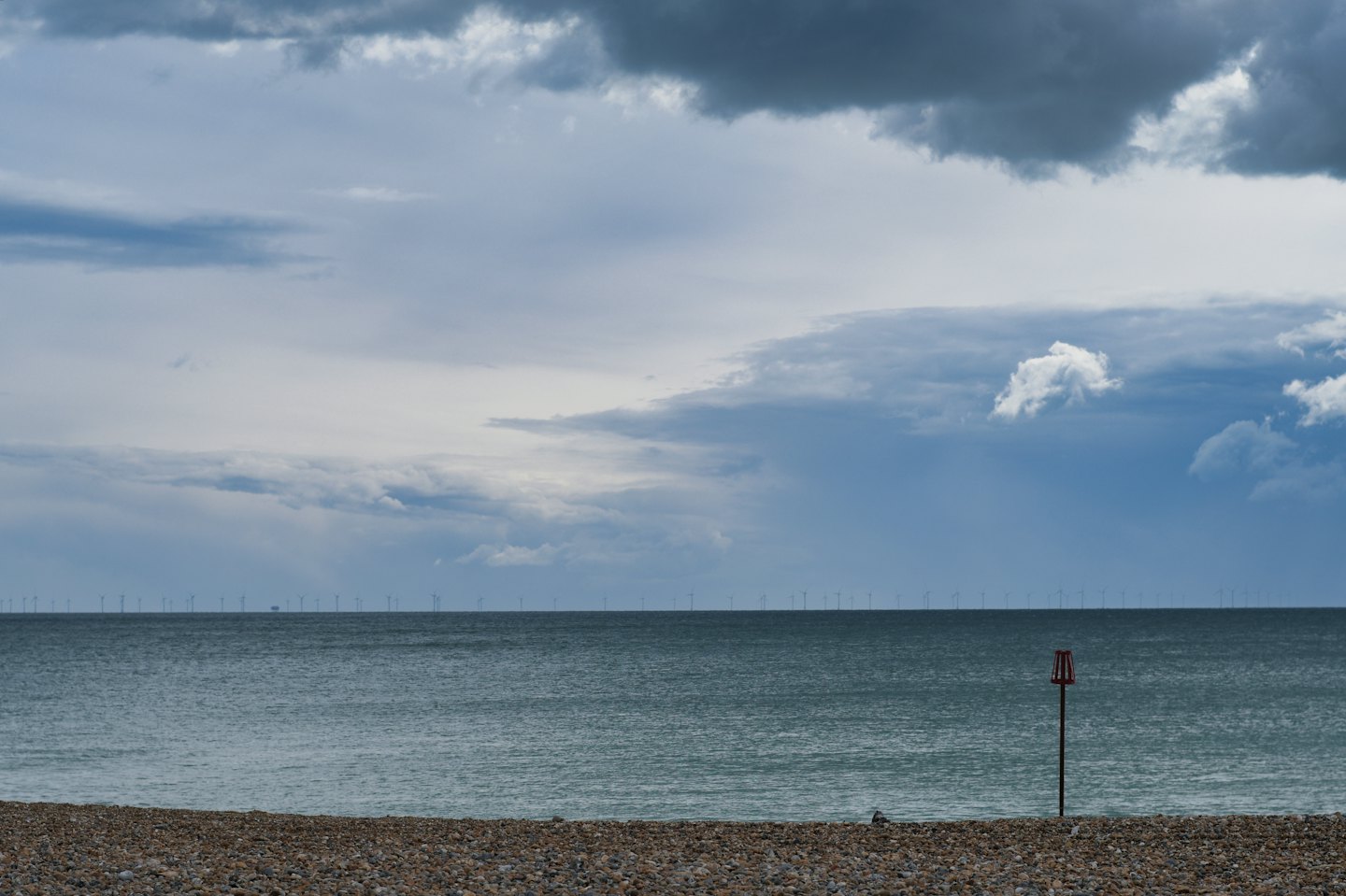 Vor der grauen Kieselbucht erheben sich Offshore-Windkraftanlagen.