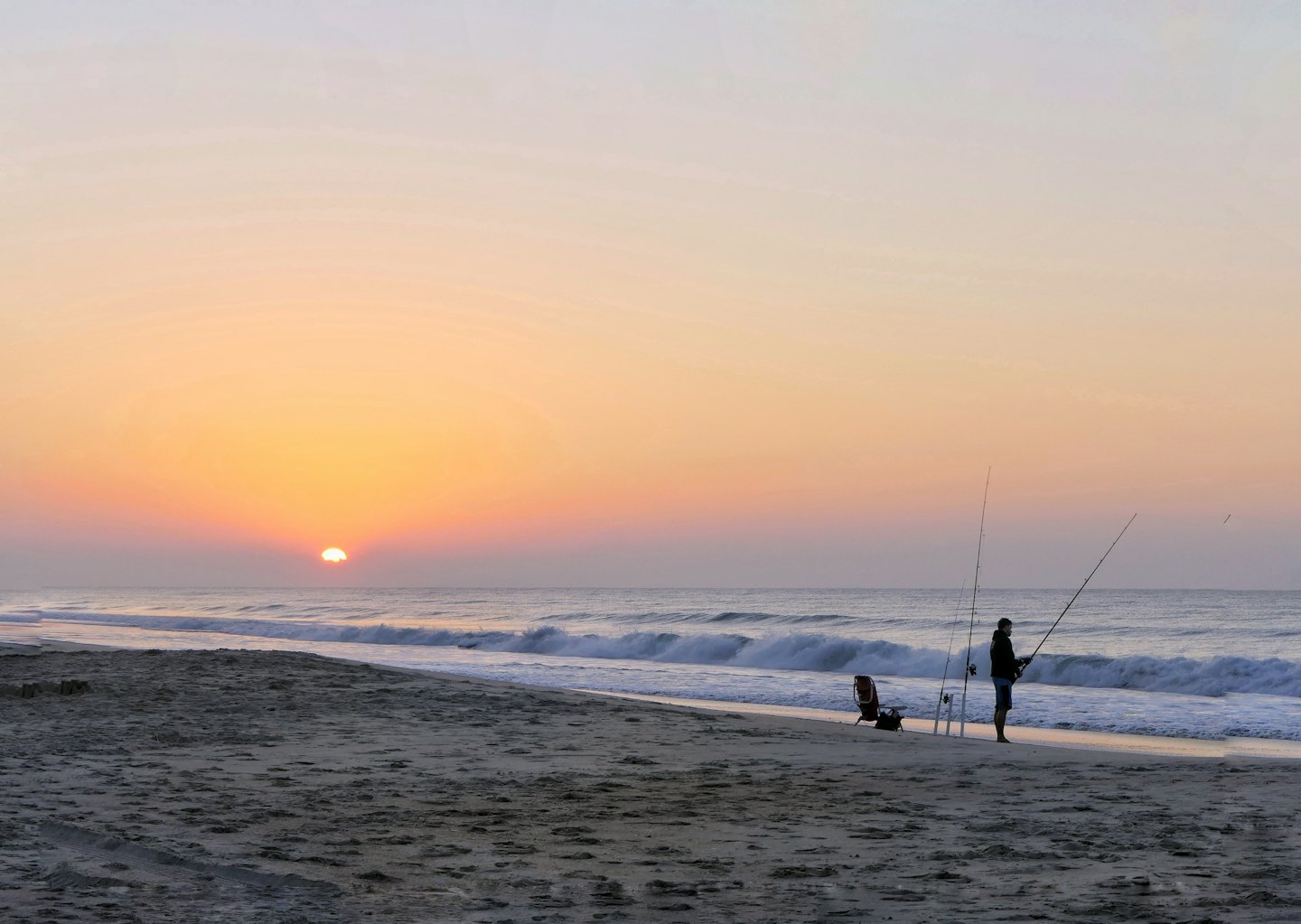 Angler am Strand bei Sonnenaufgang mit brechenden Wellen.